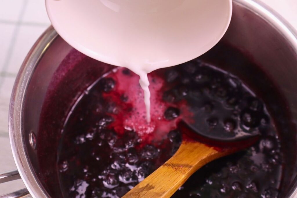 Adding arrowroot slurry to kettle of blueberry sauce to thicken it