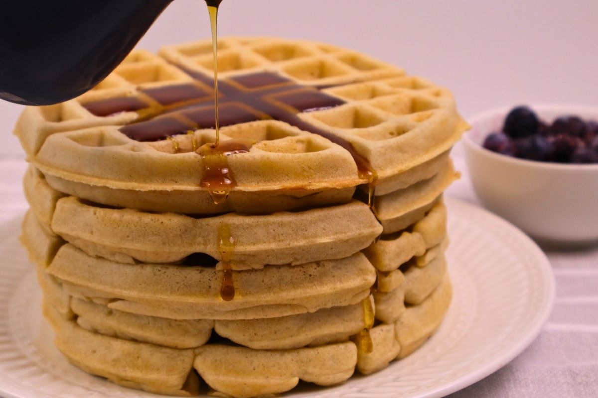 Crispy Buckwheat Waffles (Gluten-Free, Dairy-Free, From Scratch) 6 A pitcher pouring maple syrup over a stack of crispy buckwheat waffles.