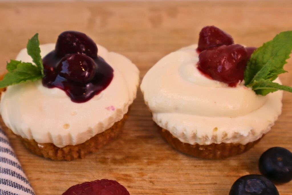 Gluten-Free Mini No-Bake Cheesecakes with Berry Sauce 20 Two gluten free mini no bake cheesecakes side by side, one topped with homemade mixed berry sauce and one with strawberry sauce, both garnished with fresh mint leaves.