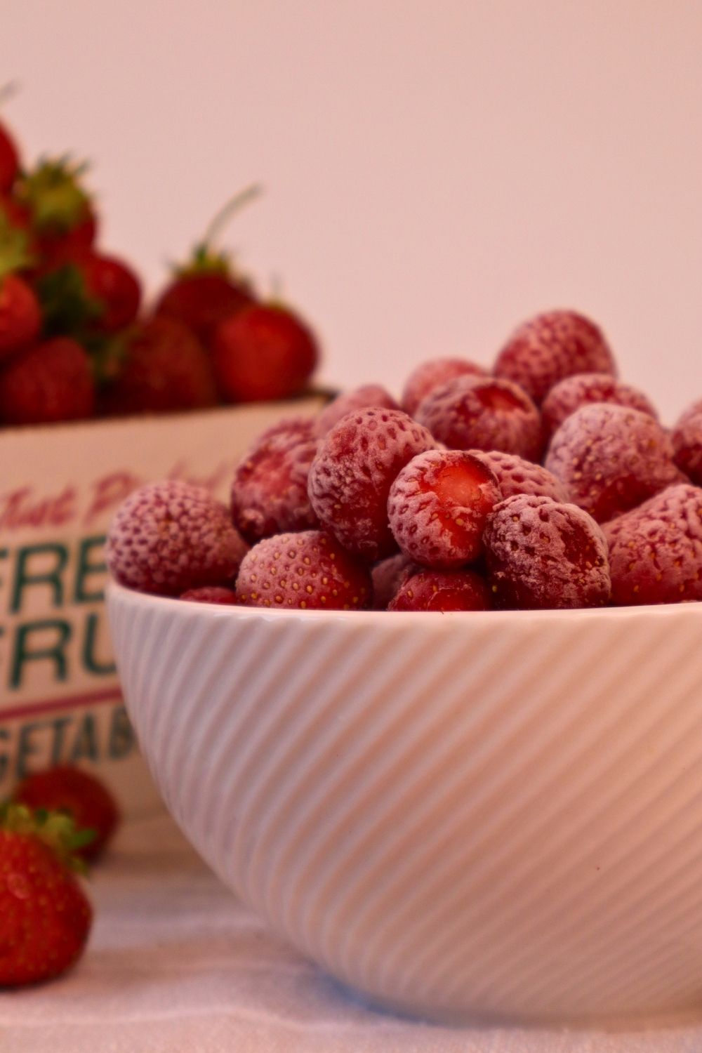 How to Freeze Strawberries (The Best Way to Preserve Fresh Berries) 15 Frozen strawberries with fresh harvest in the background - how to freeze strawberries straight from the garden or farmers market