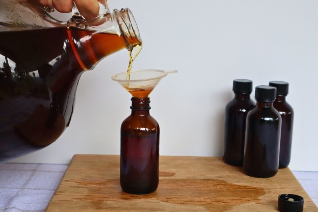 Large Batch Homemade Vanilla Extract Recipe with Vodka 13 Pouring large batch homemade vanilla extract through a funnel into small glass bottles