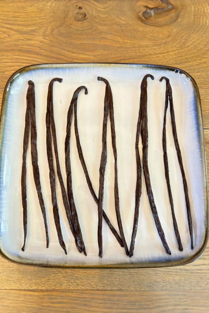 Large Batch Homemade Vanilla Extract Recipe with Vodka 9 Vanilla beans cut in half laying on a plate before making homemade vanilla extract