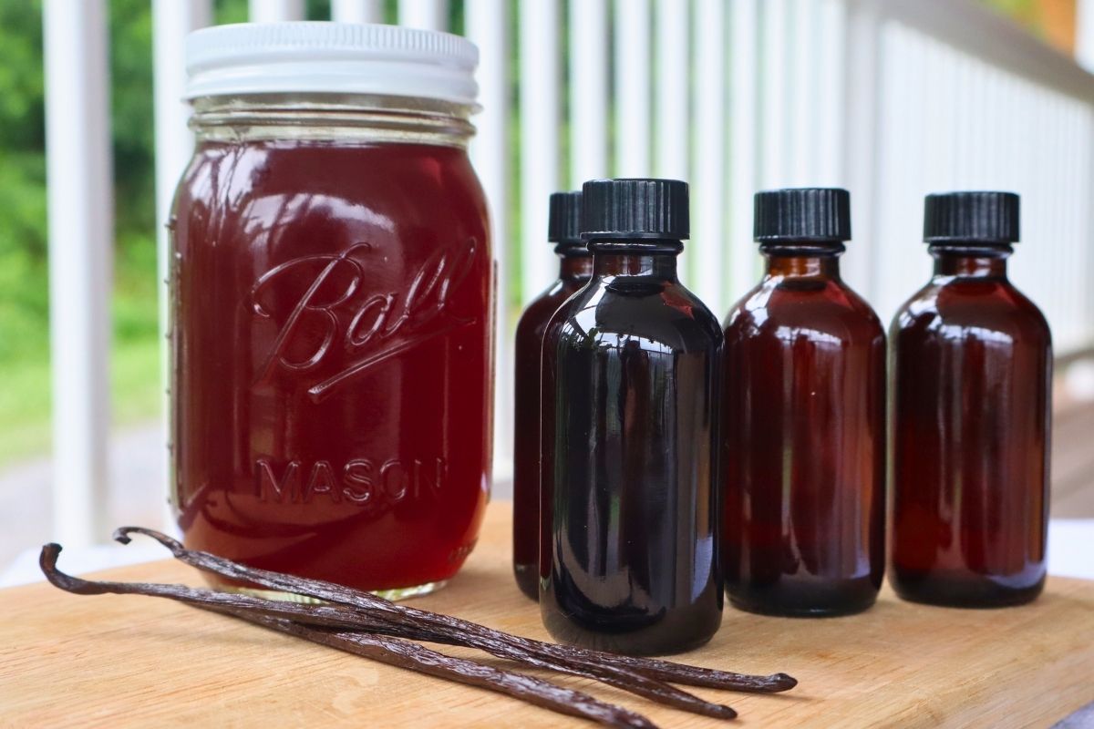 Pint jar and small glass jars of homemade vanilla extract with vanilla beans in the foreground