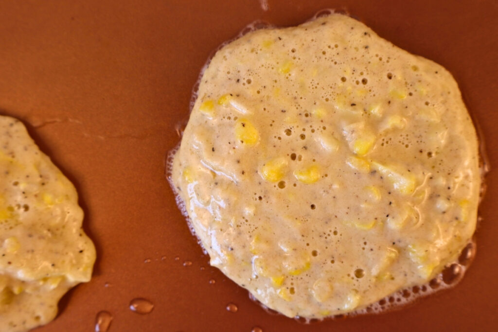 Gluten-Free Pennsylvania Dutch Corn Fritters 12 Corn fritter batter cooking on a hot griddle with bubbles forming on the surface