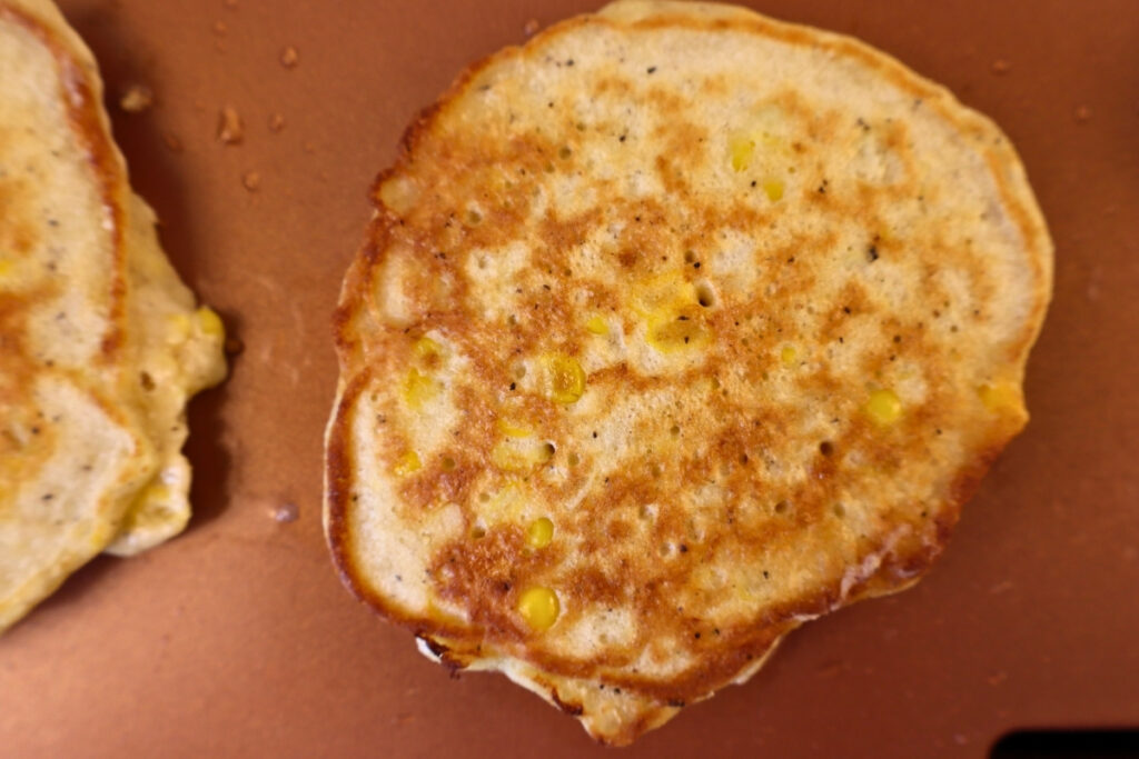 Gluten-Free Pennsylvania Dutch Corn Fritters 14 Golden brown gluten-free corn fritter cooking on a griddle