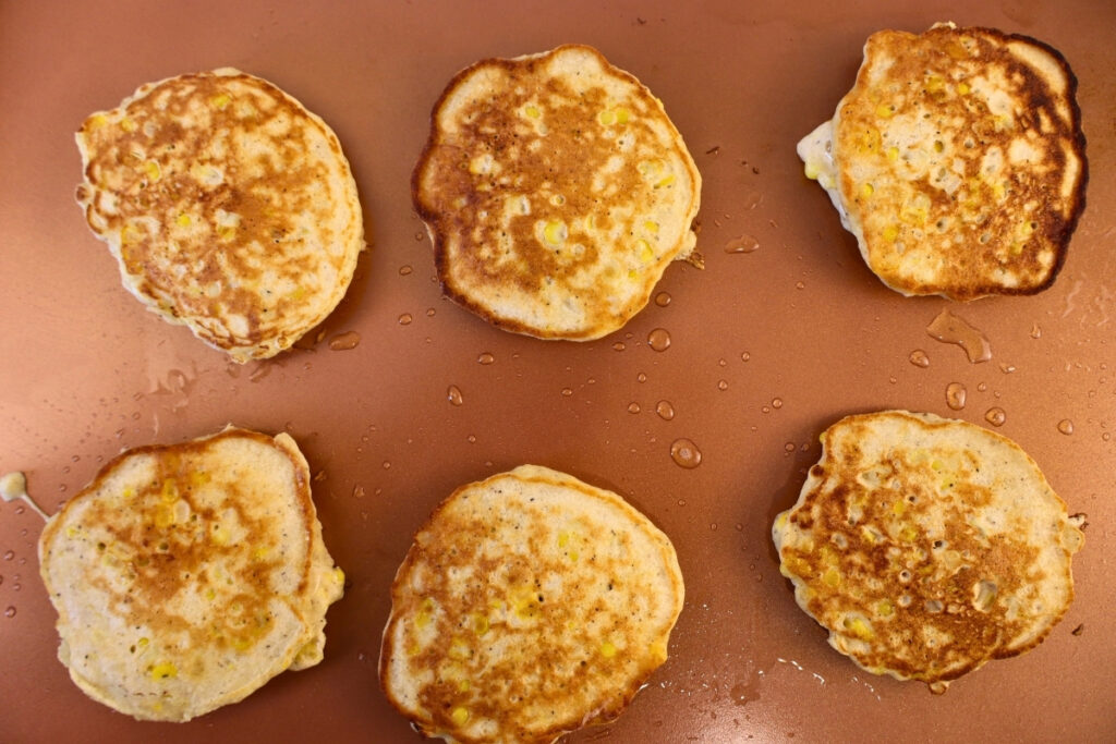 Gluten-Free Pennsylvania Dutch Corn Fritters 13 Six gluten-free Pennsylvania Dutch corn fritters cooking golden brown on a griddle