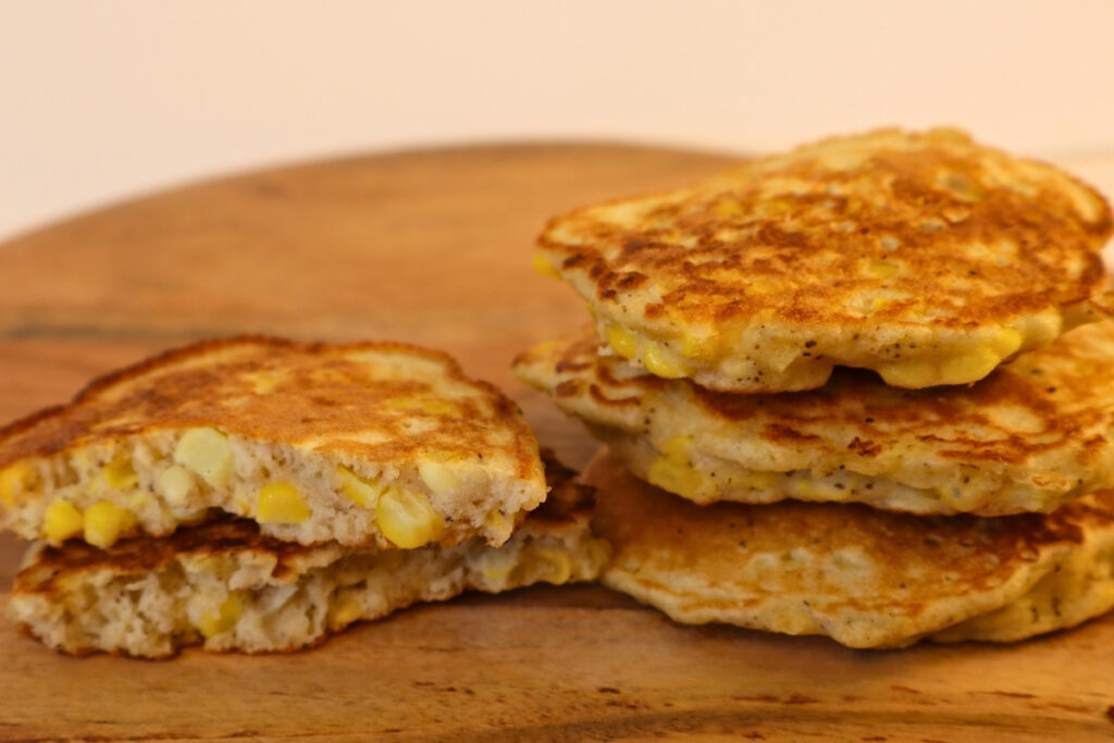 Gluten-Free Pennsylvania Dutch Corn Fritters 18 Stack of gluten-free Pennsylvania Dutch corn fritters on a wood cutting board with one split open
