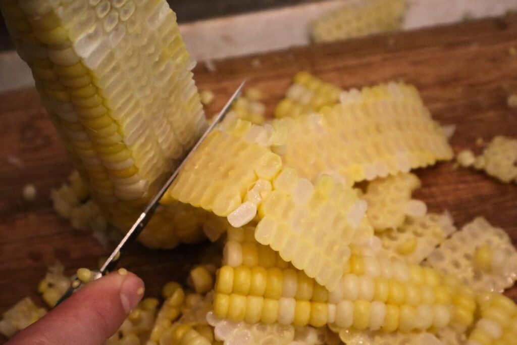 How to Freeze Sweet Corn: A Step-by-Step Preservation Guide 12 Cutting fresh sweet corn kernels off the cob with a knife on a cutting board