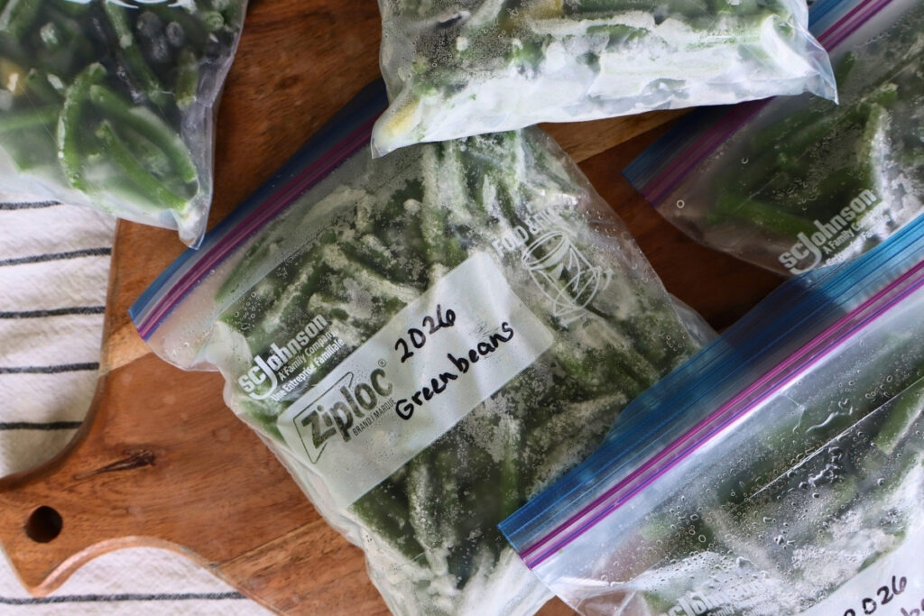 How to Freeze Fresh Green Beans From the Garden 4 Freezer bags filled with frozen green beans laying scattered on a wooden cutting board