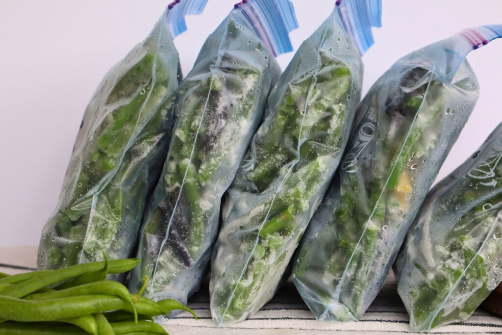 How to Freeze Fresh Green Beans From the Garden 5 Freezer bags of green beans standing upright next to a pile of fresh green beans