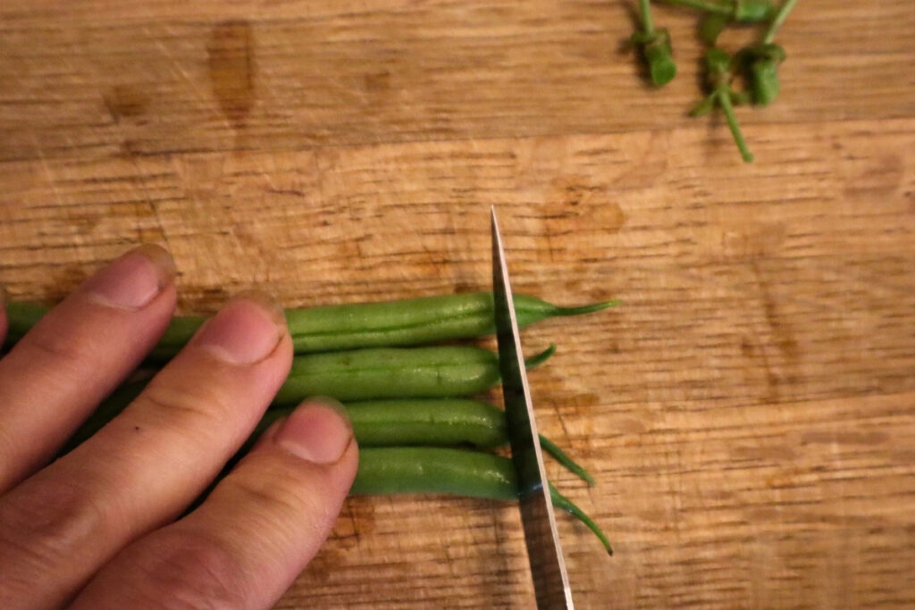 How to Freeze Fresh Green Beans From the Garden 7 Knife trimming the ends off a row of fresh green beans on a wooden cutting board